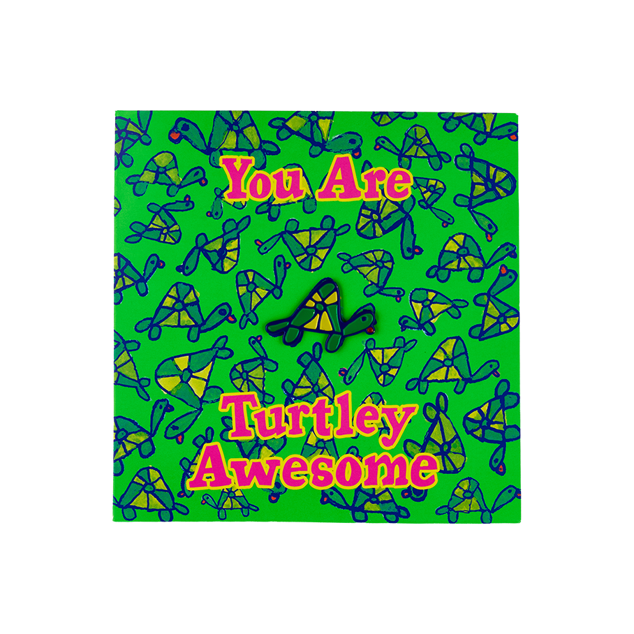 Turtley Awesome. A vibrant enamel pin in the shape of a green and yellow turtle is mounted on a matching, square green backing card with a repeating turtle pattern. Bold pink text on the card reads, 'You Are Turtley Awesome'.